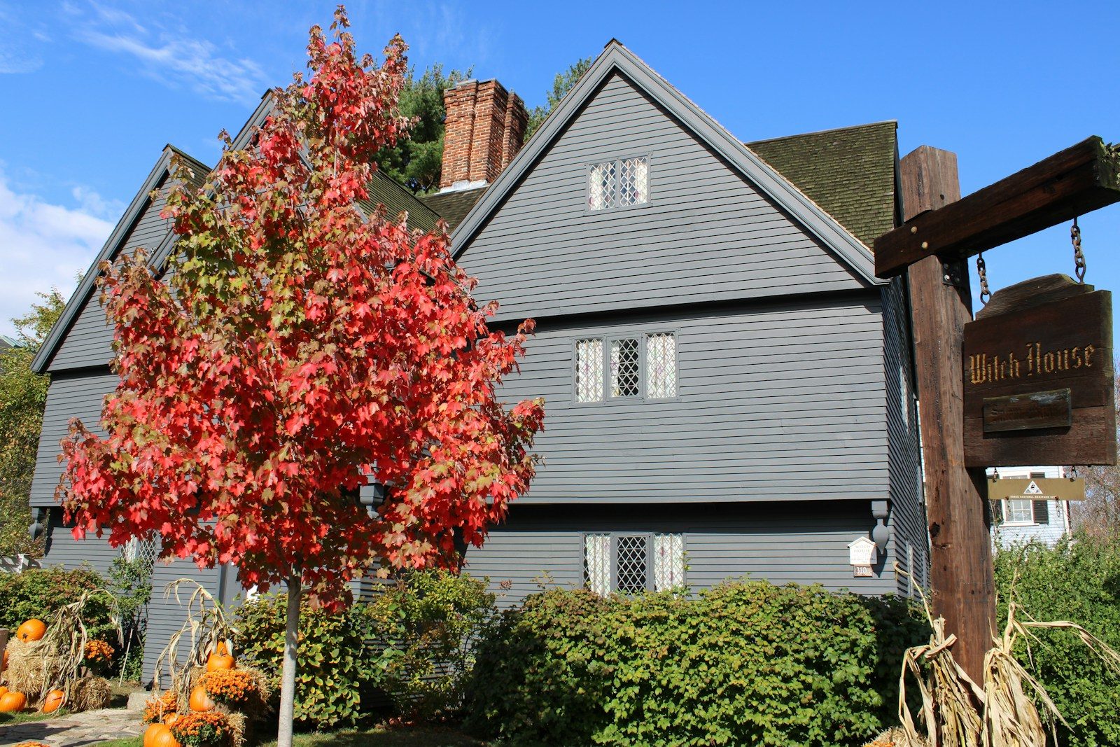 Historic gray house with autumn foliage and pumpkins.