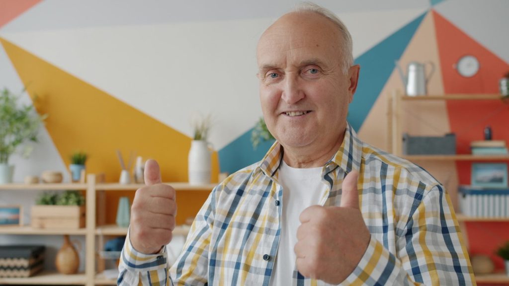 Smiling older man gives two thumbs up.